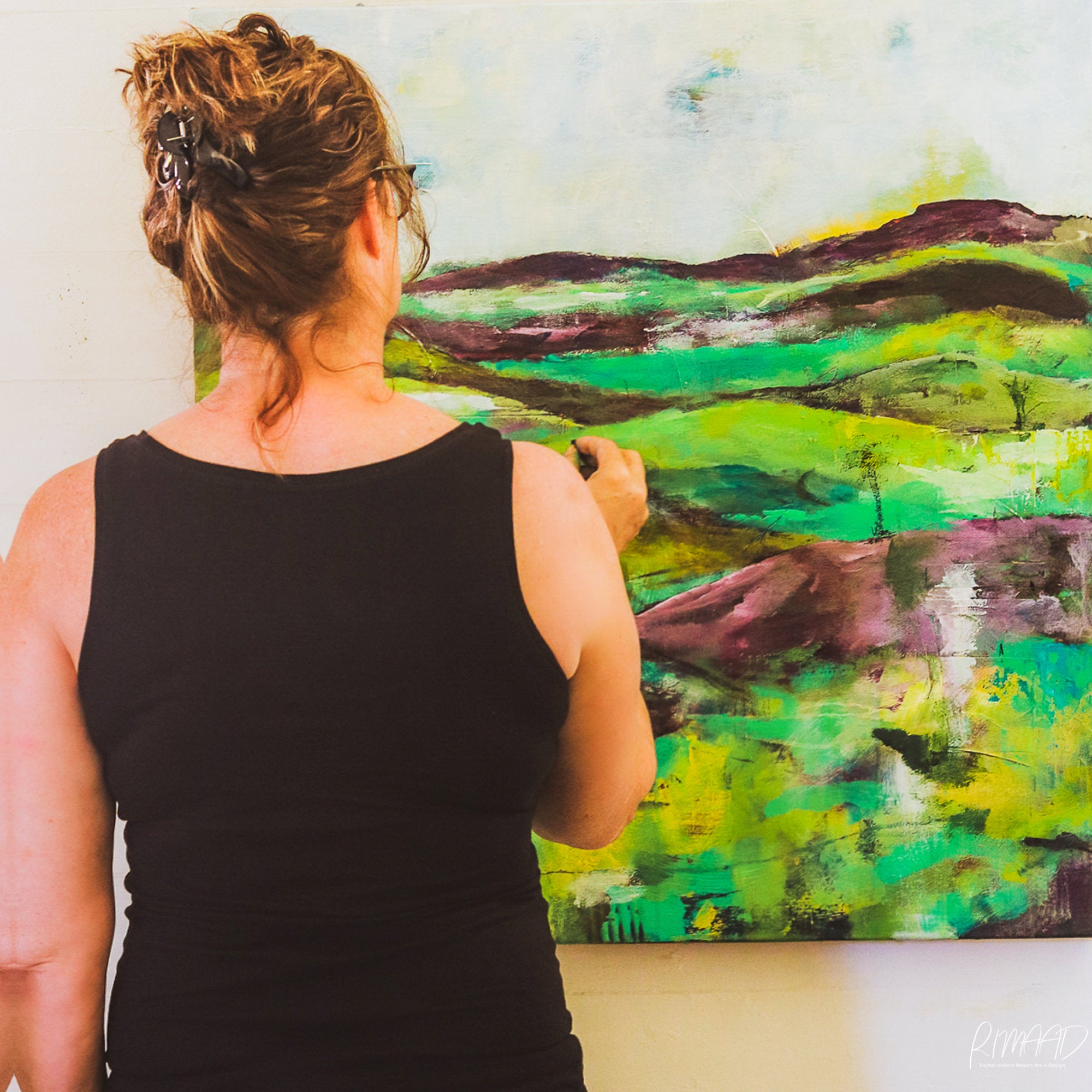 This is a photo of a woman in front of a canvas, painting. This is artist, Rachel Ireland Meyers at RIMAAD, Far North Queensland, Australia